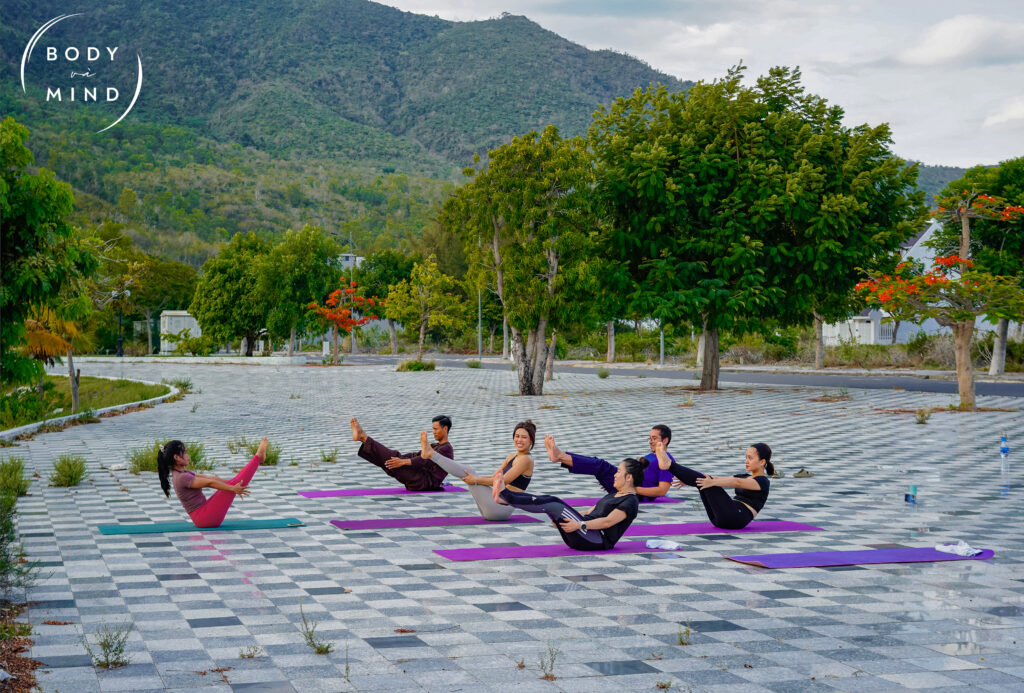 A group of Vietnamese women and men practicing yoga during sunset near the lake at BodyvaMind, a surf, yoga, and art retreat in Vietnam, surrounded by golden light