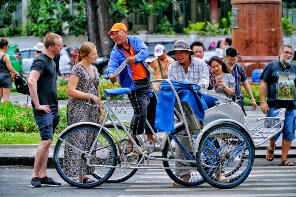 Street scene of cyclo riders and pedestrians in bustling Ho Chi Minh City, Vietnam.