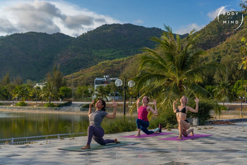 three guests at the BodyVaMind Surf Yoga and Art Retreat practice Hatha Yoga during sunrise at the lake